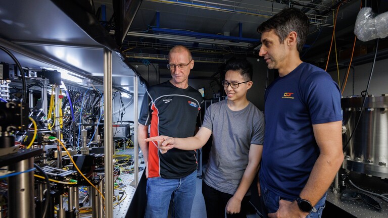 Die Forscher Murray Barrett, Michael Lee und Kyle Arnold zeigen auf die Atomuhr