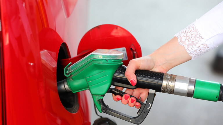 Nahaufnahme der Hand einer jungen Frau mit rotlackierten Fingernägeln, die mit einer grünen Zapfpistole Sprit in ein rotes Auto tankt