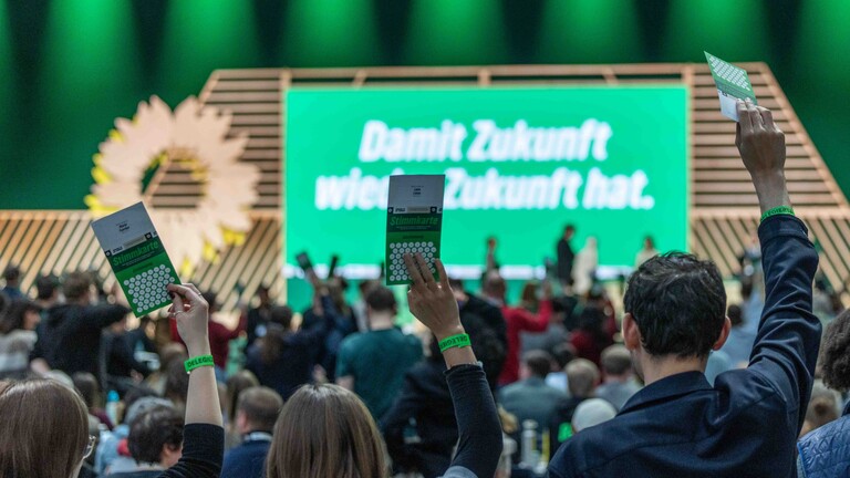 Foto von Delegierten der 51. Bundesdelegiertenkonferenz von Bündnis 90/Die Grünen am 29.11.2025 in der Messe Hannover, die vor der Parteitagsbühne Stimmkarten zur Abstimmung hochhalten