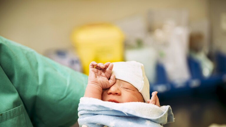 Ein Neugeborenes ist in ein Handtuch eingewickelt, es wird von einer Schwester gehalten, im Krankenhaus.