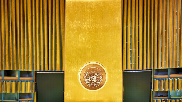 Leerer Plenarsaal der Vereinten Nationen in New York City. Blick auf das Rednerpult, die Wand dahinter ist golden.