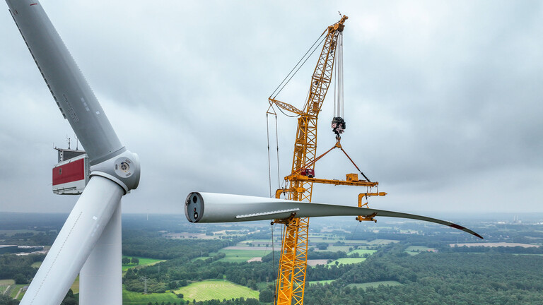 Ein mobiler Kran hebt ein Rotorblatt zum Maschinenhaus einer Windenergieanlage. (Windpark Große Heide in Dorsten,17.08.2023)