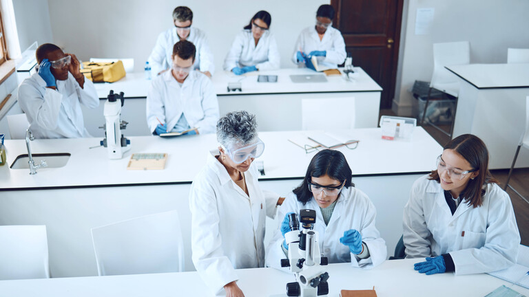 Studierende und Lehrperson in einem Raum mit Mikroskopen.
