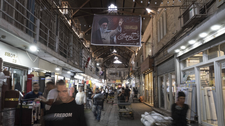 Iranische Lastträger transportieren Waren mit Karren unter einem Porträt des verstorbenen obersten Führers des Iran, Ayatollah Ali Khamenei, durch den traditionellen Großen Basar im Süden von Teheran, Iran. 1.9.2026