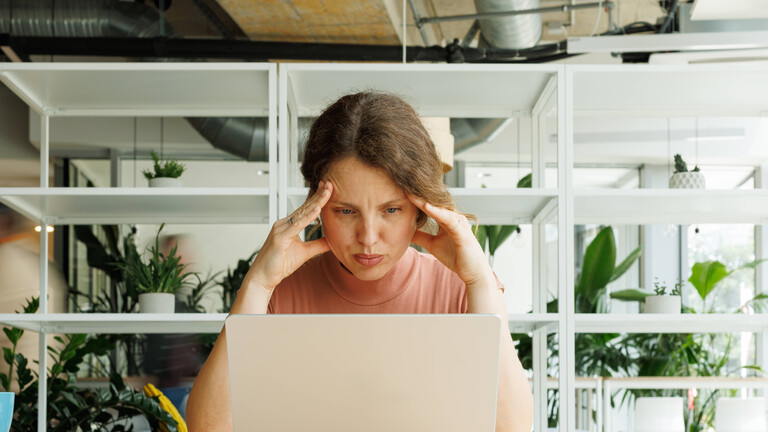 Frau am Laptop, die ihre Hände an die Schläfen hält, um sich besser zu konzentrieren.