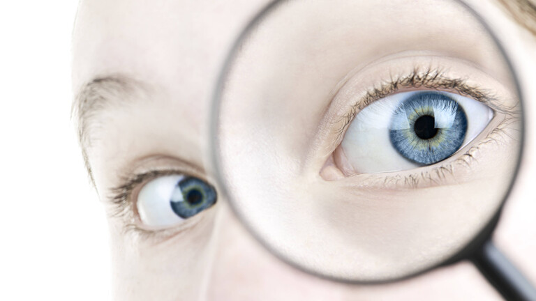 Foto eines Auges, dass durch ein Vergrößerungsglas guckt