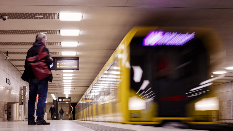 Foto einer U-Bahn-Station mit einer ausfahrenden gelben U-Bahn, die durch die Schnelligkeit unscharf erscheint, und wenigen wartenden Menschen am Bahnsteig