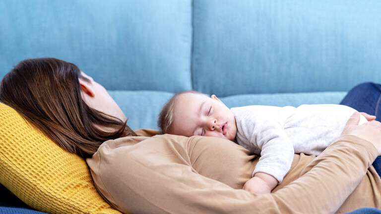 Schlafendes Baby liegt auf schlafender Frau auf dem Bauch