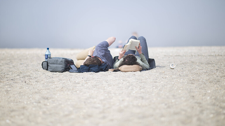 Touristen liegen im Urlaubsort Schillig am Strand im Sand. Eine der beiden Personen liest ein Buch