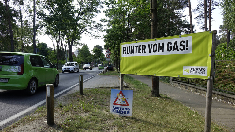 An einem Straßenrand in Fichtenwalde steht ein Transparent mit dem Schriftzug "Runter vom Gas".