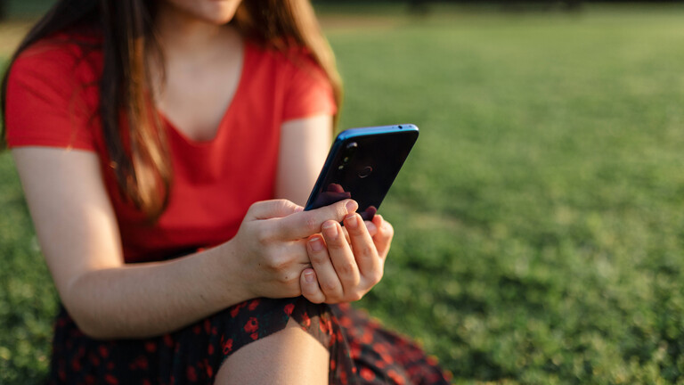 Frau mit Smartphone auf einer Wiese.
