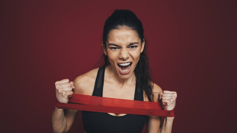 Foto einer jungen Frau in Sportkleidung, die mit den Armen ein Gummiband dehnt und dabei schreit