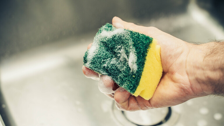 Ein Mann reinigt mit Schwamm und Spülmittel ein Waschbecken