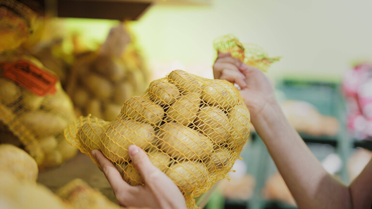 Hände greifen im Supermarkt nach einem Sack Kartoffeln