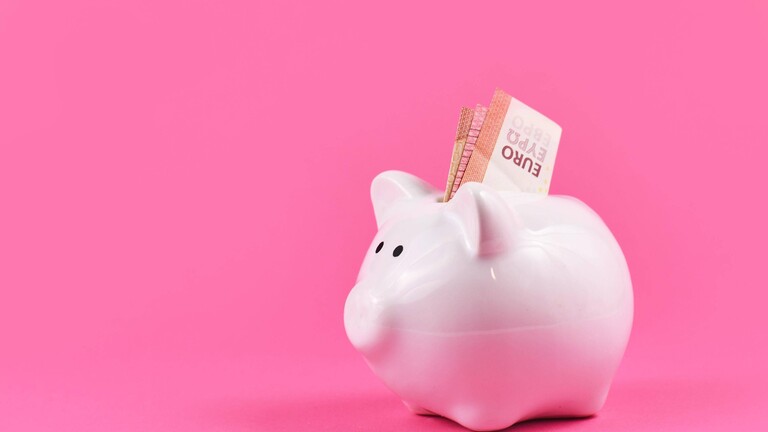 Foto eines rosa Sparschweins vor einem pinken Hintergrund, aus dem ein Zehn-Euro-Schein ragt.