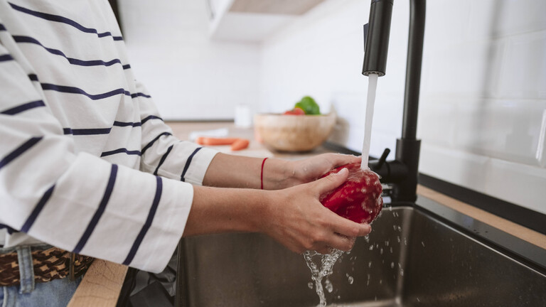 Eine Frau wäscht eine Paprika unter fließendem Wasser