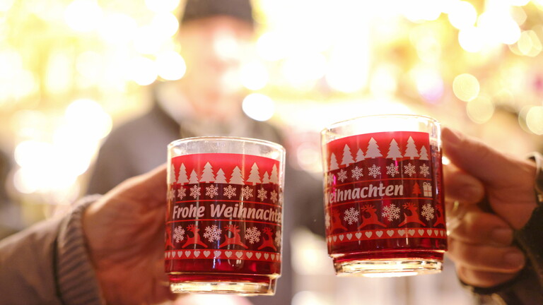 Zwei Menschen stoßen mit Glühwein an auf dem Glühweinstand auf dem Bonner Weihnachtsmarkt am Friedensplatz (2022)