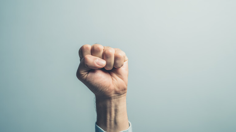 Nahaufnahme einer männlichen Hand, die zur Faust geballt nach oben gestreckt ist