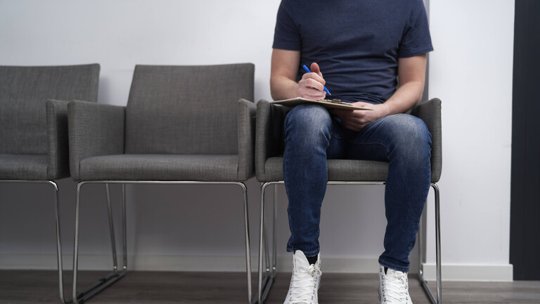 Ein Mann sitzt im Wartezimmer und füllt einen Fragebogen aus.
