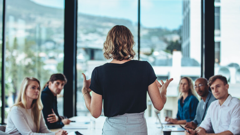 Foto einer jungen Frau von hinten, die ein team-Meeting in einem modernen Büroraum leitet