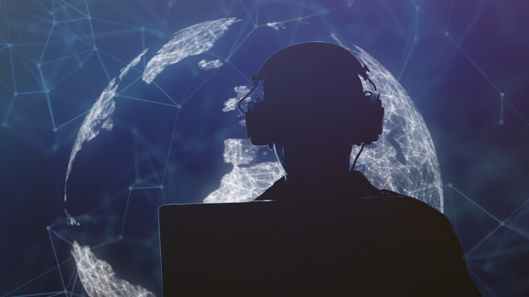 Silhouette eines Mannes mit Kopfhörer vor einem Laptop vor dem Hintergrund eines großen Bildschirms, auf dem der Erdball grafisch dargestellt ist mit Verbindungslinien darauf, die den Eindruck digitaler Vernetzung erwecken