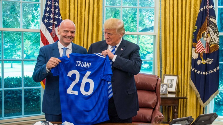US-Präsident Donald Trump hält ein blaues WM-Trikot hoch, neben ihm steht FIFA-Präsident Gianni Infantino. Die beiden halten sich im Oval Office im Weißen Haus auf.