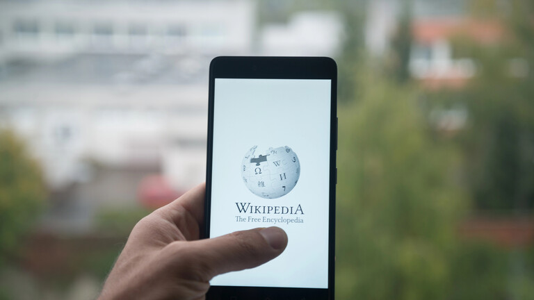 Eine Hand, die ein Smartphone hält, auf dem Wikipedia geöffnet ist.