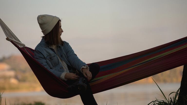 Eine Frau chillt auf einer Hängematte in der Abendsonne. Sie wirkt nachdenklich.