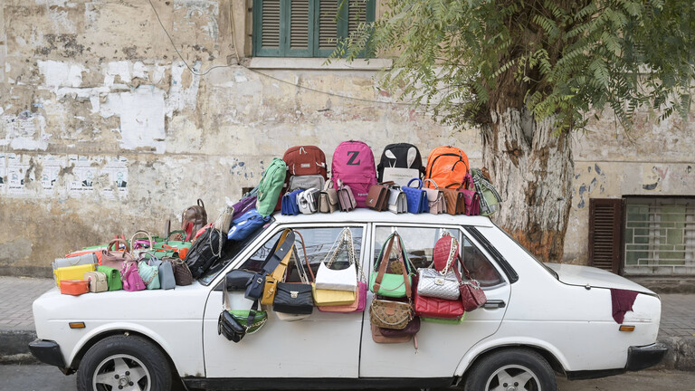 Auf einem alten weißen Auto stehen auf Dach und Autohaube viele bunte Taschen, auch an den Fenstern hängen Taschen. Es sind Fake-Taschen, die zum Verkauf angeboten werden, in der ägyptischen Stadt Assiut.