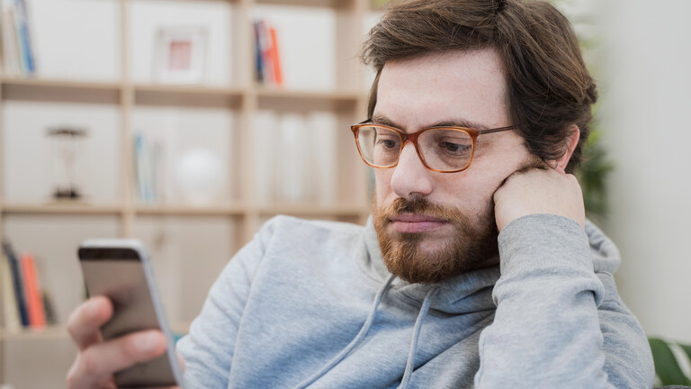 Ein Mann blickt deprimiert auf sein Smartphone