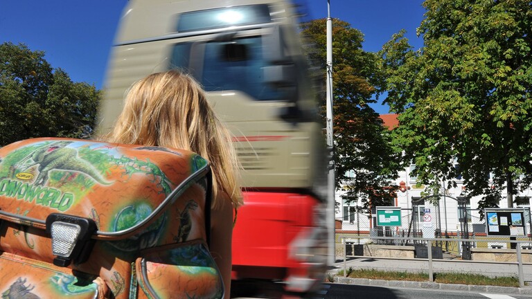 Mädchen mit Schulranzen am Zebrastreifen, riesiger LKW prescht vorebi