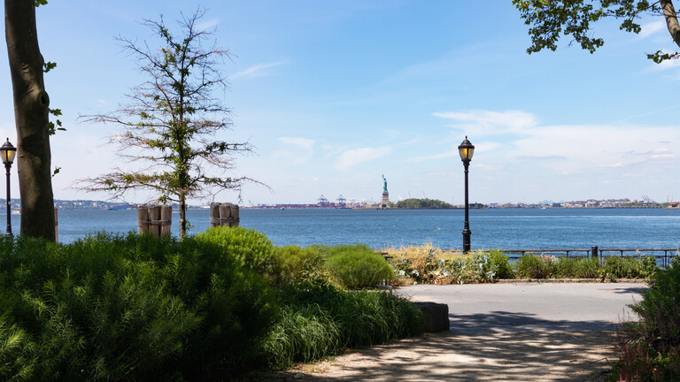 Blick von der Südspitze Manhattans auf die Freiheitsstatue von einem Park aus.