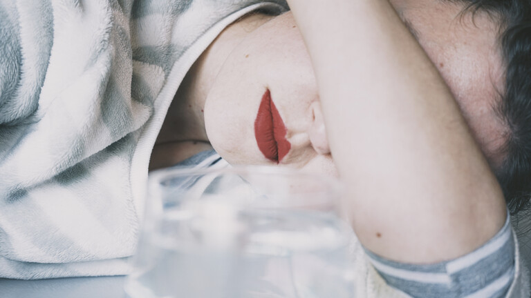 Eine junge Frau verdeckt ihre Augen mit ihrem Arm, vor ihr ein Glas