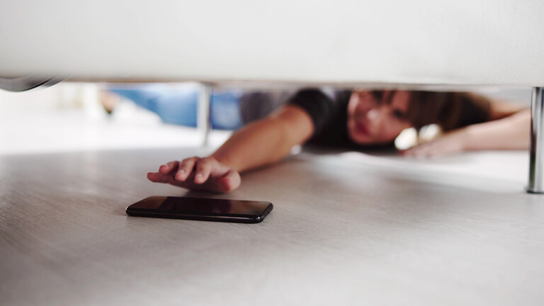 Eine Frau greift nach einem Smartphone unter der Couch.
