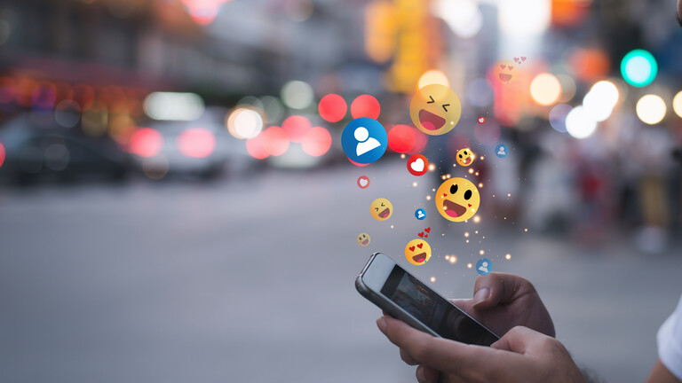 Mensch tippt auf Smartphone, Emojis fliegen heraus