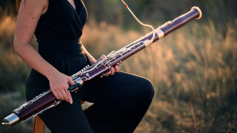 Eine Frau sitzt bei Sonnenuntergang auf einer ruhigen Wiese und hält ein Fagott in den Händen