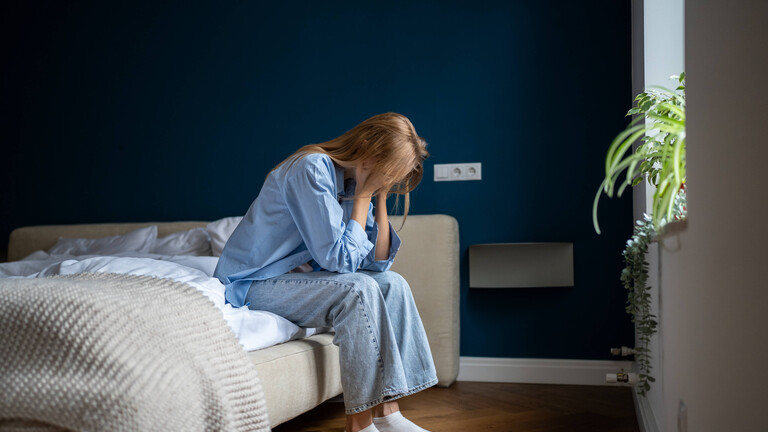 Eine Frau sitzt auf dem Bett im Schlafzimmer und stützt ihr Gesicht in die Hände