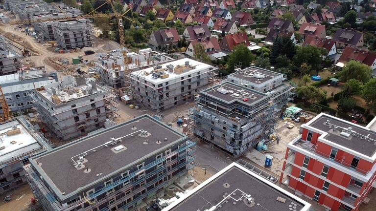 Baustelle für einen Neubau von Mehrfamilienhäusern mit Kran im Hintergrund und Einfamilienhäuser an der Seite (Berlin, 2028)