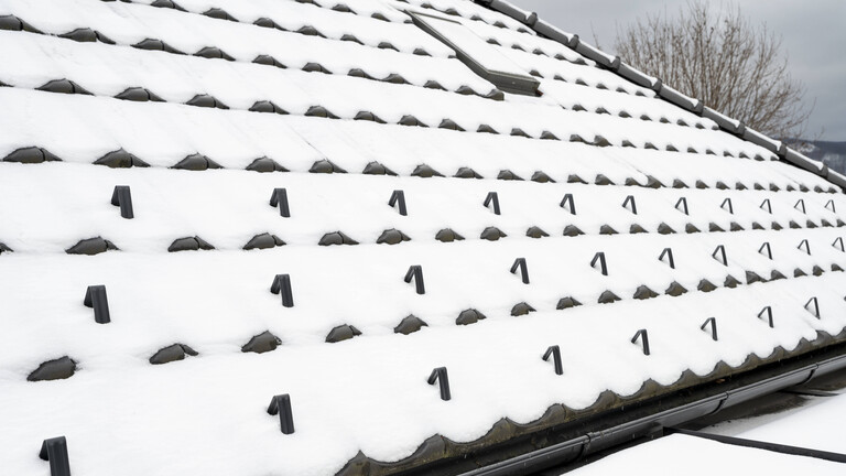 Schneehaken auf einem schneebedeckten Ziegeldach