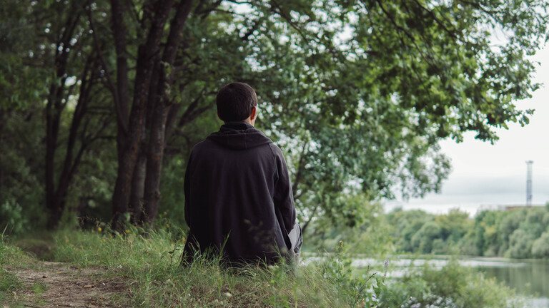 Ein junger Mann sitzt nachdenklich an einem Flussufer