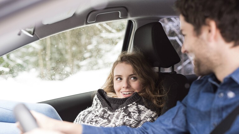 Autofahrer und Beifahrerin lächeln sich an