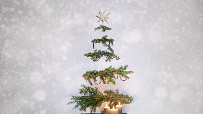 Tannenbaumzweige mit Dekoration hängen an der Wand in Form eines Tannenbaums