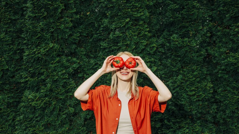 Eine Frau hält sich eine Paprika und eine Tomate vor die Augen