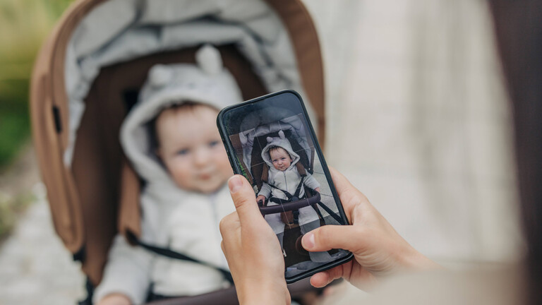 Eine Frau macht mit ihrem Handy ein Foto von einem Baby im Kinderwagen.