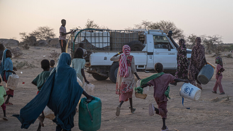 Foto von sudanesischen Flüchtlingen im Tschad, die mit Behältern zu einem Lastwagen laufen, um Wasser zu bekommen
