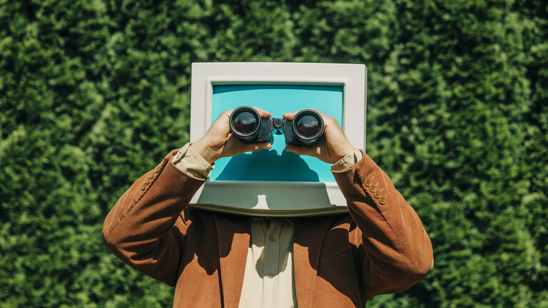 Person mit einem Retro-Monitor-Kopf, die im Freien ein Fernglas benutzt.