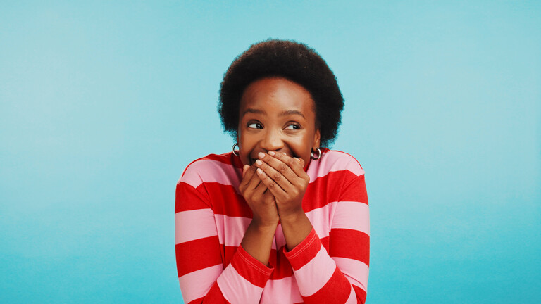 Foto einer jungen Frau, die ihre beiden Hände vor den Mund hält, um ein Lachen zu verbergen