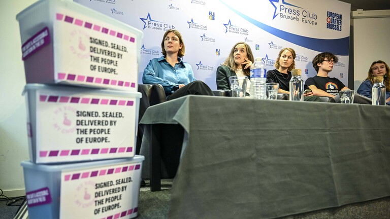 Bei einer Pressekonferenz der Bürgerinitiative "My Voice, my Choice" am 1. Oktober 2025 sitzen Personen auf einer kleinen Bühne, ganz vorne im Bild stehen Plastikboxen gestapelt. Vermutlich sind die Unterschriftenlisten darin enthalten.
