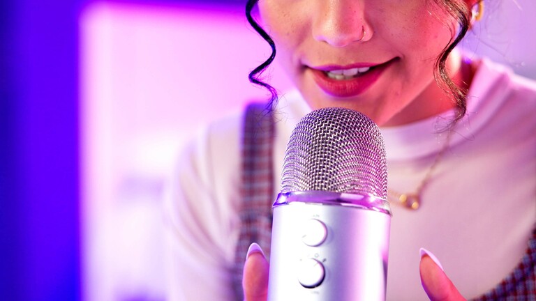 Eine Frau steht an einem Mikrofon und spricht. Ihr Gesicht ist nur im Ausschnitt zu sehen.