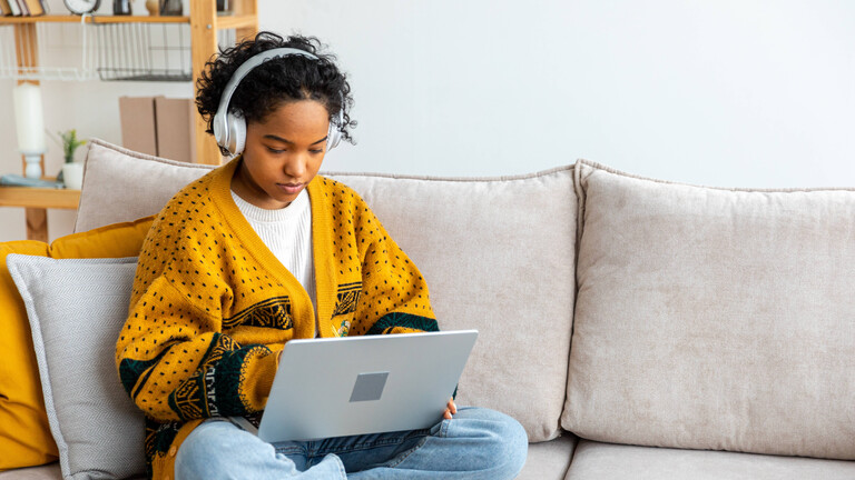 Frau mit Kopfhörern auf Sofa sitzend schaut auf Laptop